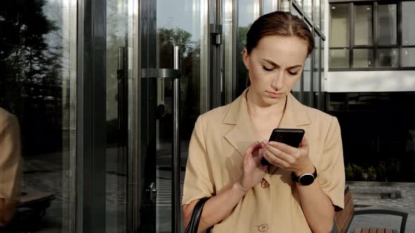 Adult Caucasian Confident Young Business Woman is Talking on Phone Outside near Modern Building