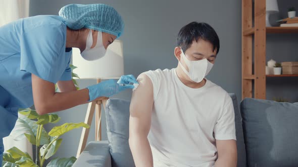 Young Asia lady nurse giving Covid-19 or flu antivirus vaccine shot to male patient.