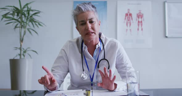 Caucasian female doctor at desk talking and gesturing during video call consultation