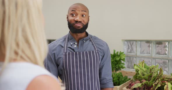 Video of happy african american salesman showing organic vegetables to caucasian female customer