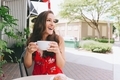 A happy woman smiling while drinking a cup of coffee on an outdoor patio.  - PhotoDune Item for Sale