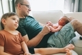 A father sitting on the couch with his newborn baby and son.  - PhotoDune Item for Sale