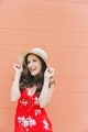 A beautiful happy woman wearing a red summer dress and sun hat, smiling against an orange wall.  - PhotoDune Item for Sale