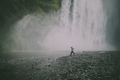A man jumping across the rocks in front of a giant waterfall.  - PhotoDune Item for Sale
