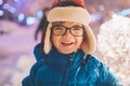 A little boy with glasses smiling in the Christmas lights on a snowy night in winter.  - PhotoDune Item for Sale