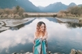 A beautiful woman with pink hair wrapped in a blanket standing in front of a mountain and lake. - PhotoDune Item for Sale