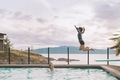 A little boy jumping off of a diving board into a pool by the ocean. - PhotoDune Item for Sale