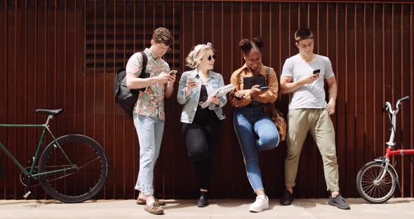 Students using smartphones, leaning on wall