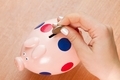 the woman's hand drops a coin into the piggy Bank - PhotoDune Item for Sale