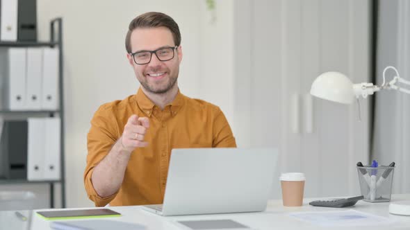 Young Man with Laptop Pointing at the Camera