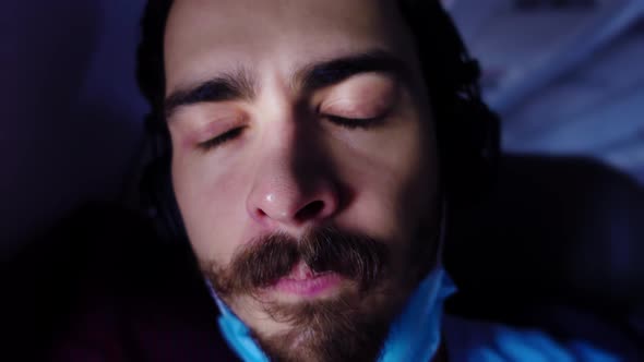 Portrait of Young Bearded Man Sitting in a Plane with Headphones and Taking Off Medical Mask