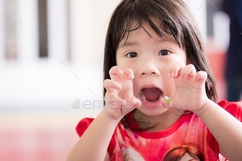  threatening and roaring at people. Happy bright Asian child plays ghost with family. Kid raised both hands to cheek and made terrifying claw pose.
