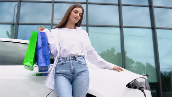 Happy Young Girl Standing on City Parking Near Electric Car Charging Automobile Battery From Small