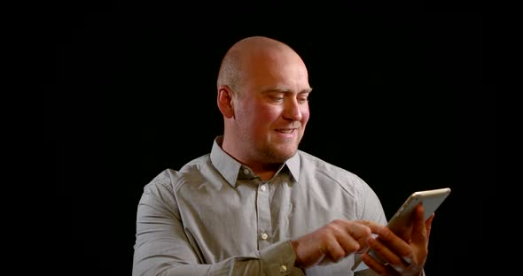 Bald Man Is Using Tablet in Black Background, Touching Sensor Screen, Switching on Video Call