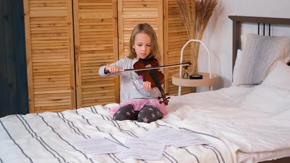 Child Girl Practicing Violin While Sitting on Bed