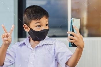 child boy wearing mask for prevent Covid-19 disease and corona virus. using a smart phone