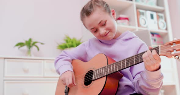 Teen Girl is Playing Guitar Sitting on the Chair in Front of the Computer