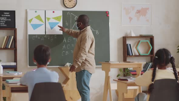 Afro-American School Teacher in Mask Giving Lesson to Kids