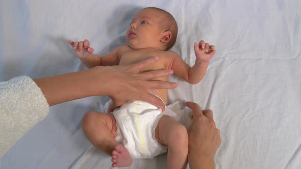 Mother Changing Diaper on Her Newborn Baby Indoors, Little Legs of a Newborn Baby, The Child Moves