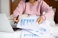 work from home, a young Asian woman who works in finance at home calculates financial graphs showing - PhotoDune Item for Sale