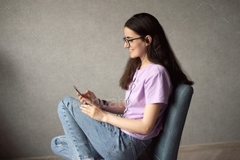 A young girl is sitting and looking at the phone with headphones