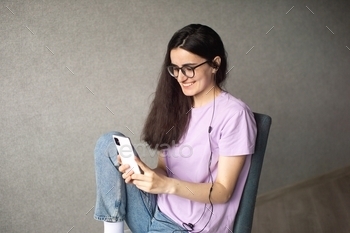 A young girl is sitting and looking at the phone with headphones