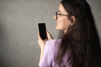 A young girl with glasses holds a phone in her hands and looks away