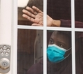 African American man wearing blue surgical mask at home looking through window  - PhotoDune Item for Sale