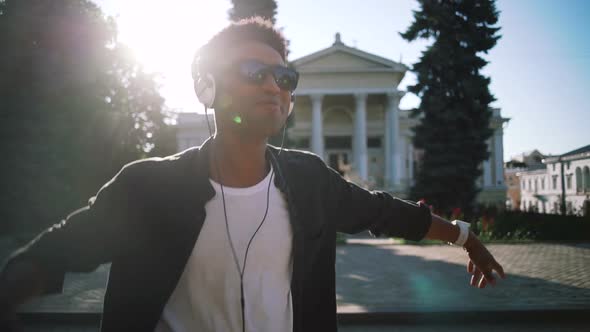 Young Stylish Hipster Black Man in White Headphones and Sun Glasses Dancing Outdoor in City Centre