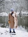 Stylish young girl in a brown coat and a blue hat admires the snow and winter. Winter nature - PhotoDune Item for Sale