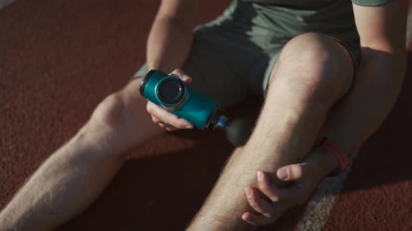 A Male Athlete Massages Muscles and Tendons with a Massage Percussion Device After a Workout at the