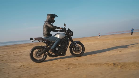 Motorcyclist Driving His Customized Fast Motorbike on the Dirt Road in Desert Around Sea or Lake