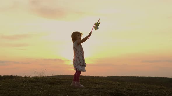 Little Girl Standing On Nature At Sunset. Girl Holding Windmill