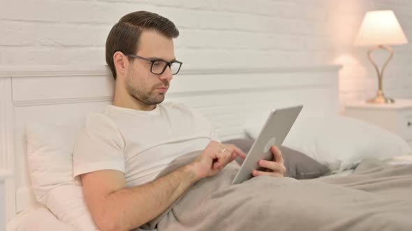 Relaxing Young Man Using Tablet in Bed