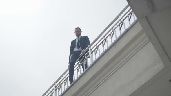 Suicidal Caucasian Man in Formal Suit and Eyeglasses Climbing Over Bridge Fence. Bottom View Wide