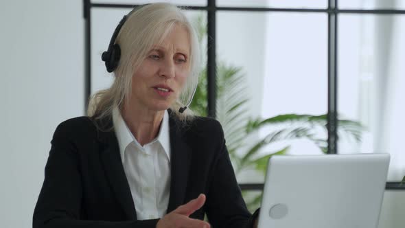 Elderly Lady in a Headset Talks on a Video Conference Conducts a Video Conference Using a Laptop in