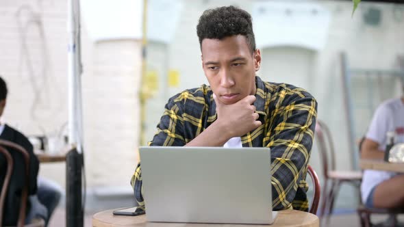 Thinking Young African Man Brainstorming and Working on Laptop