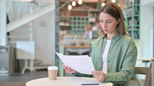 Serious Woman Reading Paperwork in Cafe 