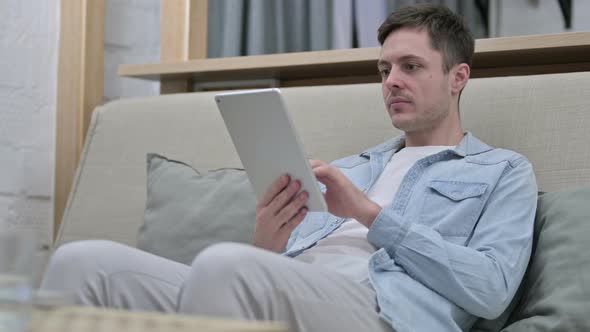 Attractive Young Man Sitting on Sofa and Using Tablet