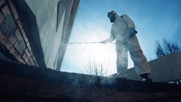 A Person in a Hazmat Suit Is Spraying Chemicals Onto a Wall