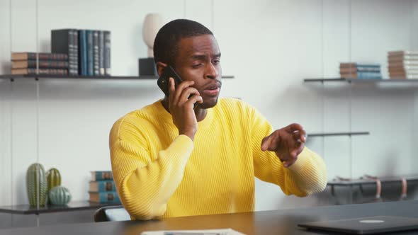 Young male talking on the smartphone while sitting at the desk in the office.