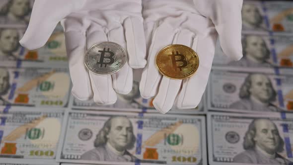 A Hand in White Gloves Holds a Golden Bitcoin on the Background of Dollar Bills