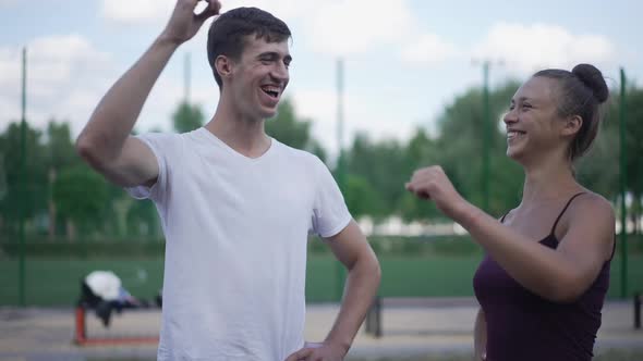 Positive Caucasian Young Man and Woman Gesturing Highfive Showing Strength Gesture Smiling Looking