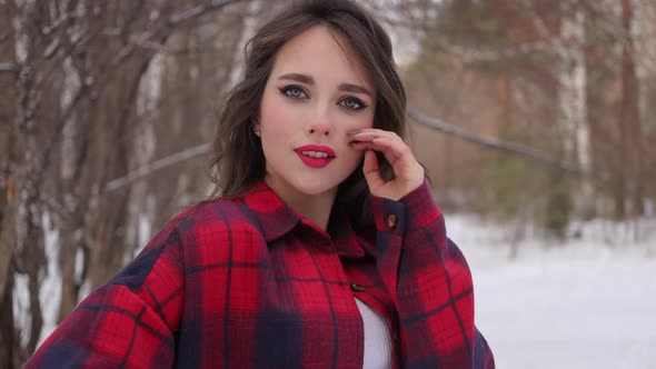 Young Woman with Wavy Hair Standing and Touching Face in Winter Forest