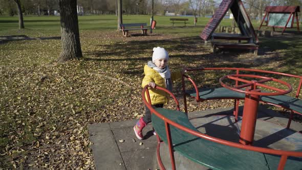 Adorable infant son playing at merry-go-round in public playground, Zagreb.