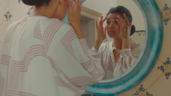 Displeased 20s African American Woman Touching Her Face Skin Looking at Mirror Standing in Bathroom