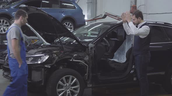 Side View of Shocked Caucasian Man Standing Next To His Broken Car As Auto Mechanic Coming Up