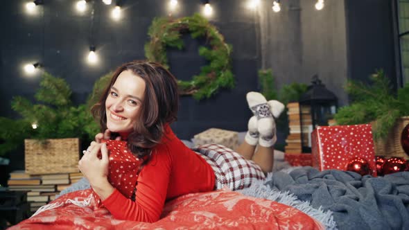 Woman in warm stylish clothes poses on bed in decorated room.