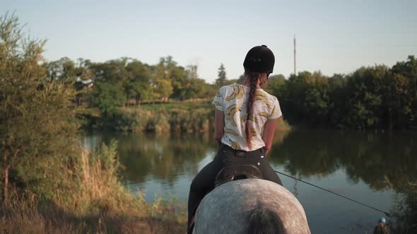 A young girl sits down to the lake while sitting on a horse. Rider in a helmet for riding. Jockey.