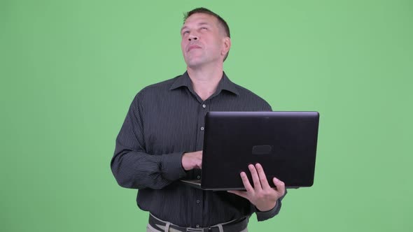 Macho Mature Businessman Thinking While Using Laptop